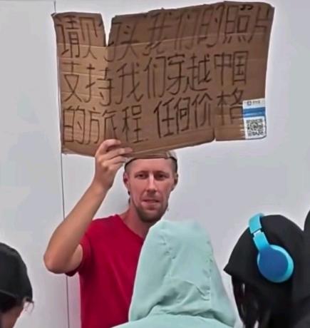 街头，有个来中国穷游的外国人，举着一张附有收款码的纸牌，期望得到大家的支持。纸