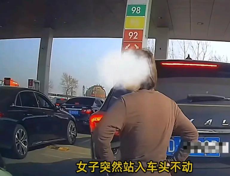 男子开车往加油站加油，中年女子突然站在车头进行人肉插队，女子突然站入车队不动，
