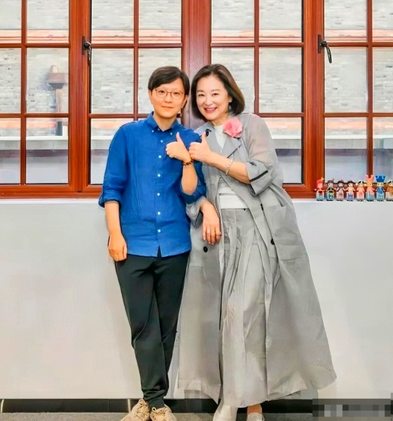 这是70岁左右的林青霞与一位女士的合影。照片里林青霞穿着浅灰色长外套裙子，别着粉