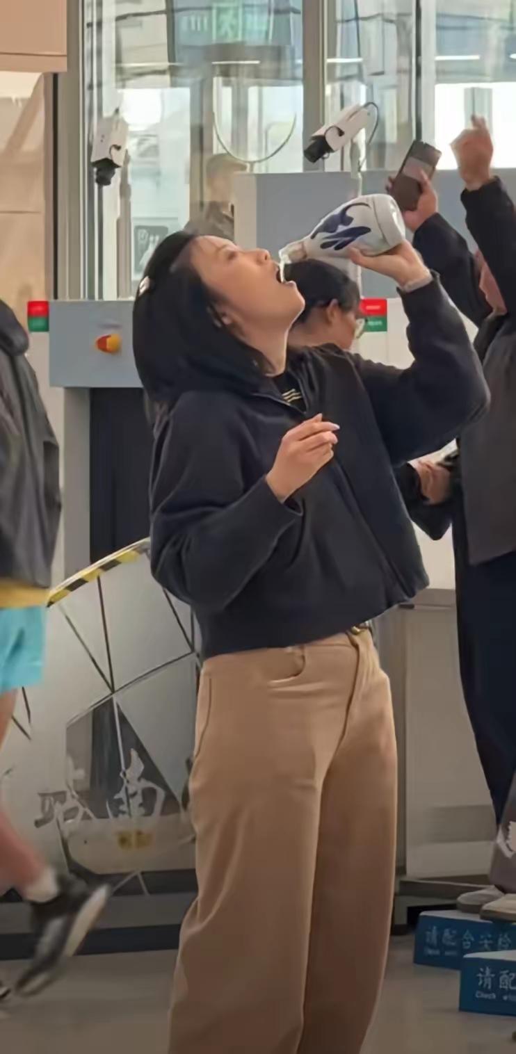 高铁安检口，一个姑娘仰起脖子，对着一瓶酒往下灌。旁边的人举着手机在拍。她没有