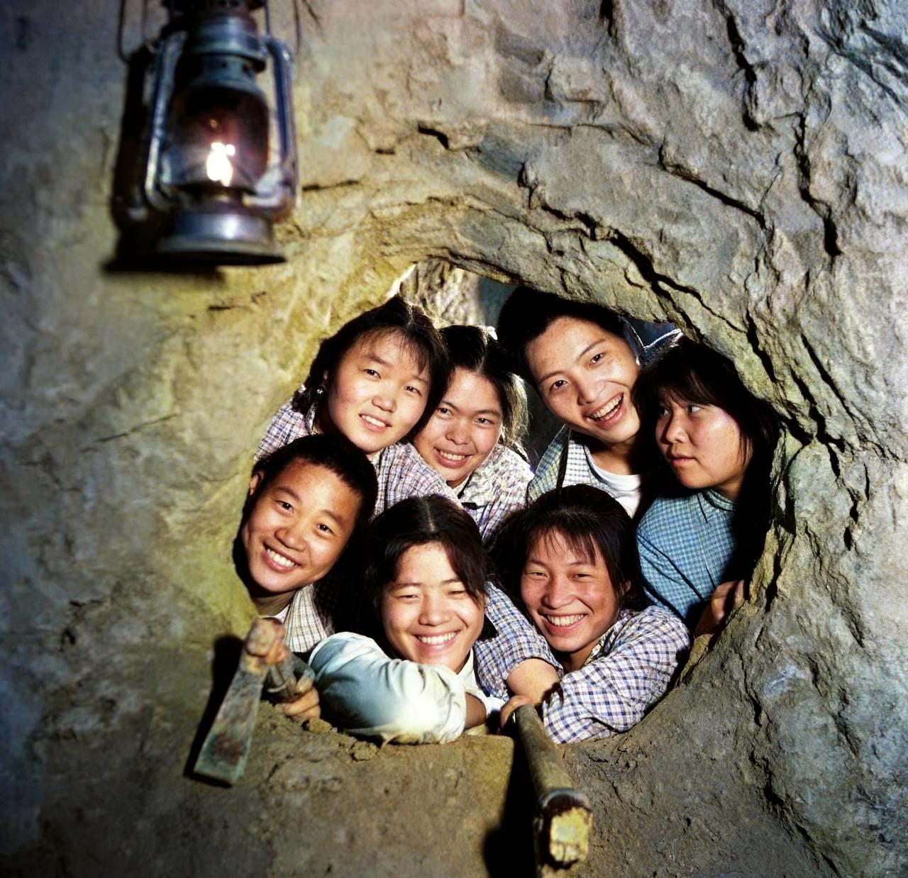 这是1969年陕西七名年轻女子挤在地道口处，脸上露出灿烂的笑容。洞口处悬挂着一盏