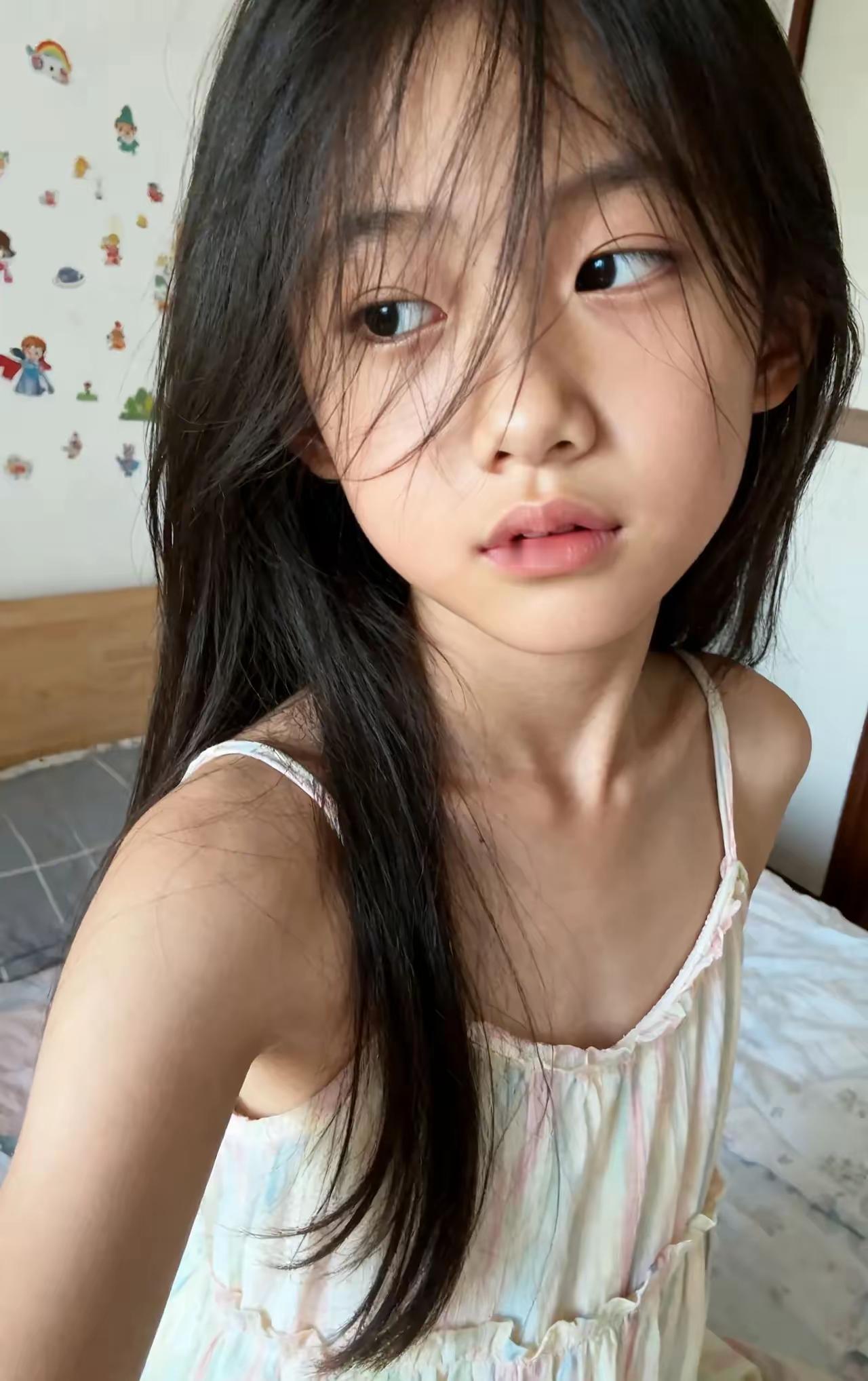 她站在贴满卡通贴的墙前，头发垂成自然的弧度，吊带裙的细肩带晃着细碎的光。没有