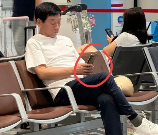网友拍到魏建军在凳子上坐着休息看手机。手机牌子看不出来，从摄像头分布看，是国产