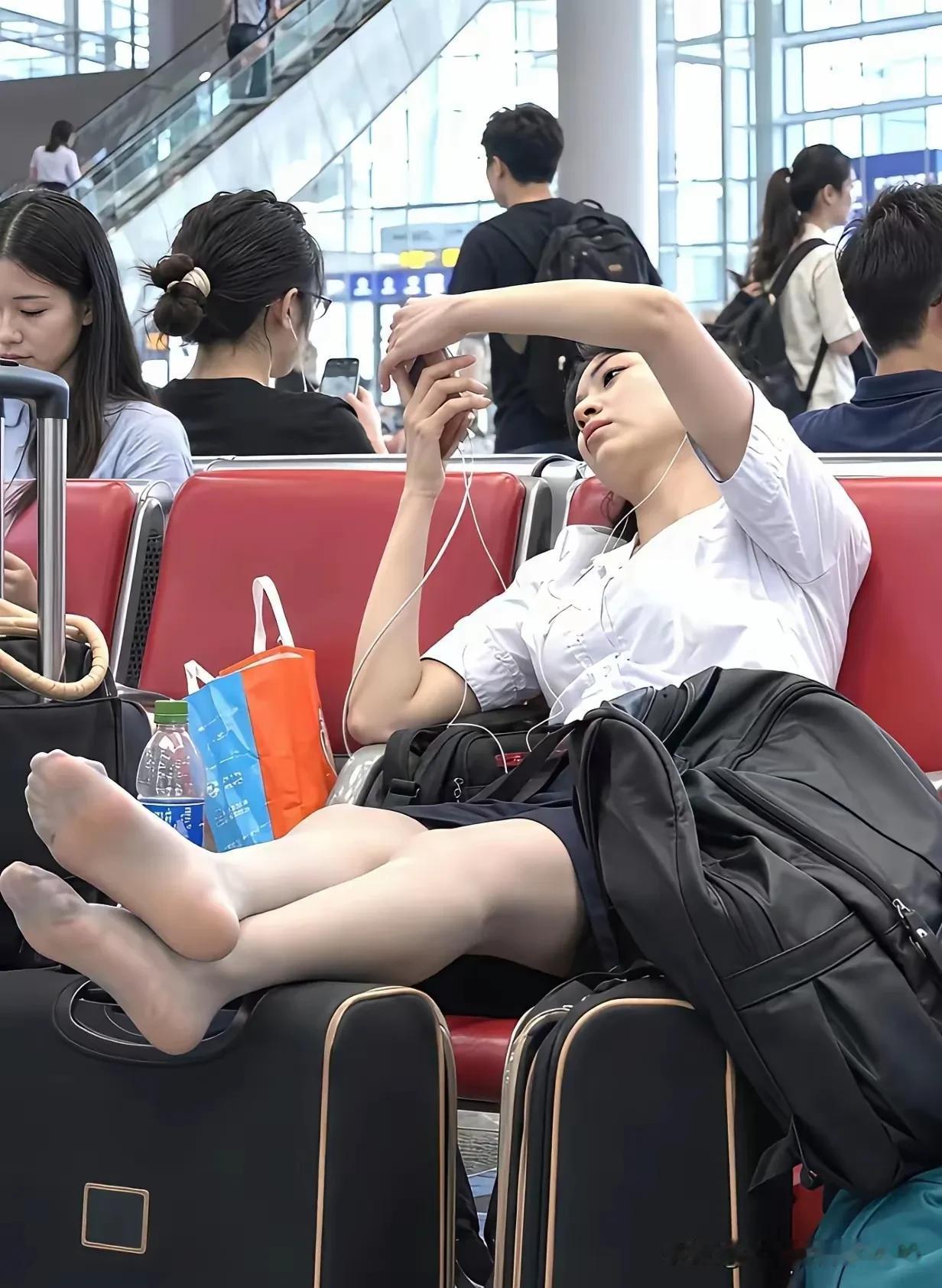 候车大厅内一名美女把鞋脱了，把脚丫子伸到到行李箱上刷手机，完全无视是在公共场合。
