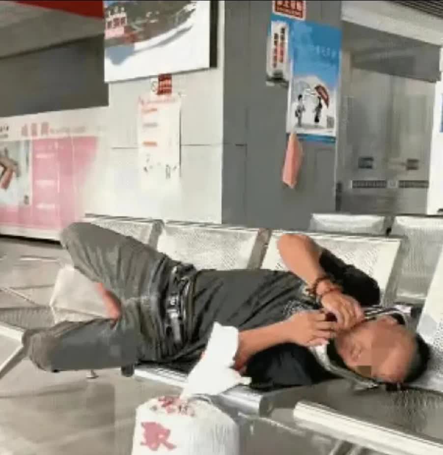 一男子在等火车，发现还有等两个小时才检票，他就躺在铁椅子上睡一会！椅子不够长