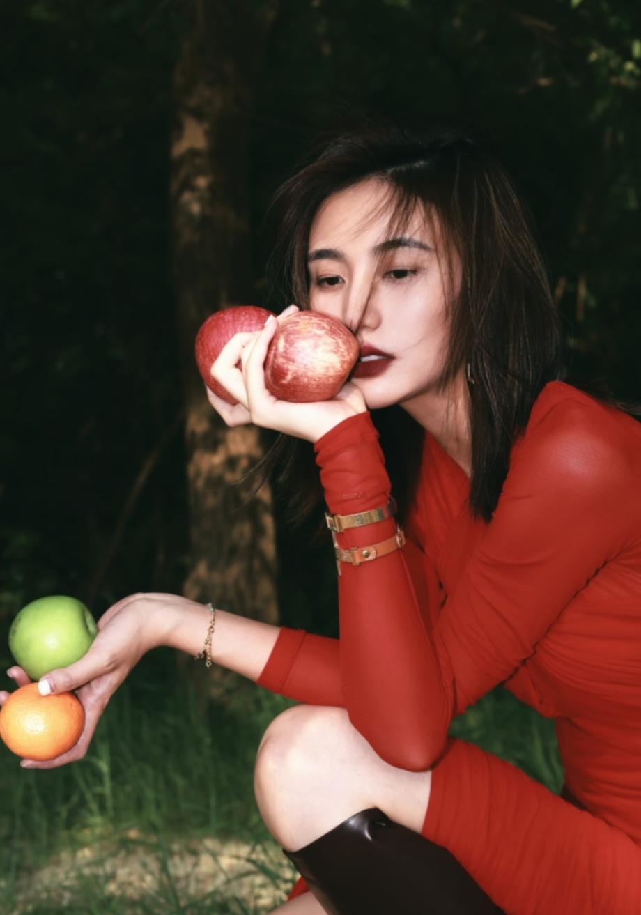李亚鹏前妻海哈金喜晒出一组照片，红色裙子配长靴，躺在草地上，嗅着手中苹果的