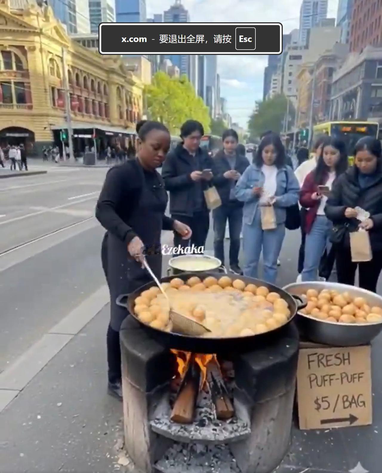 在英国伦敦街头，尼日利亚黑人女子当街烧柴火，卖油炸小吃。其背后就是伦敦的CBD