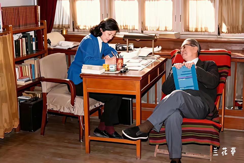 外交家乔冠华和妻子章含之的温馨时刻。章含之正在伏案工作，乔冠华坐在桌前的椅子上