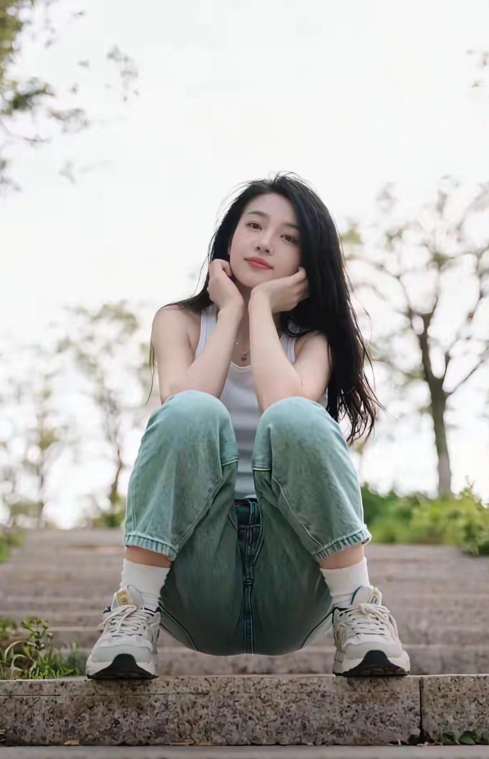 浅绿牛仔裹着松弛感，白背心衬得风都软了些。手肘撑在膝盖上托着腮，连发丝都沾着夏末