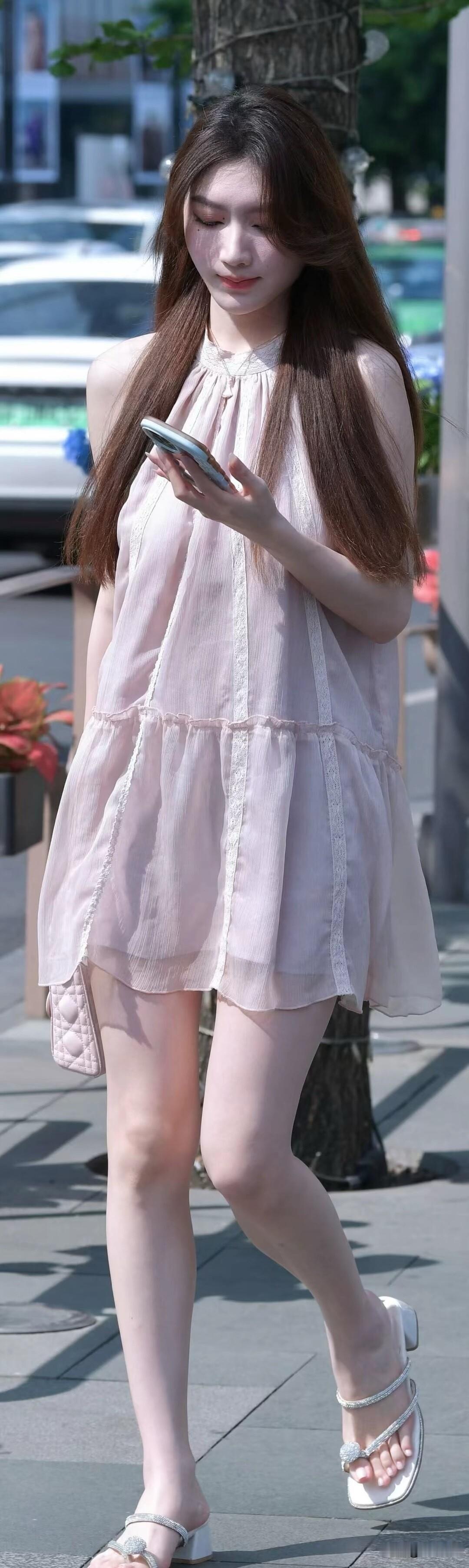 穿着粉色裙子的女孩在街上看手机。