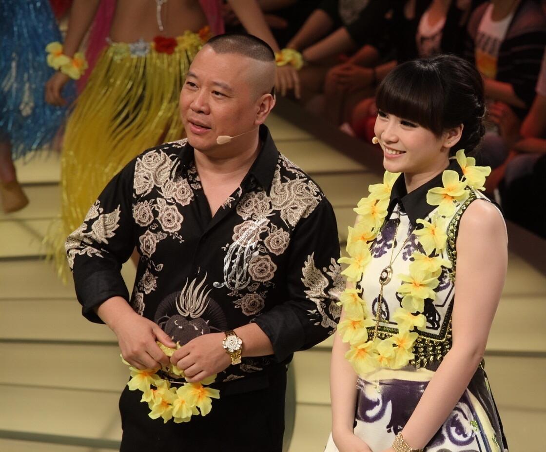 镜头中手执黄色花环的郭德纲衣着考究，发型拉风，目光如镜，气色盈和；一旁的美女刘海