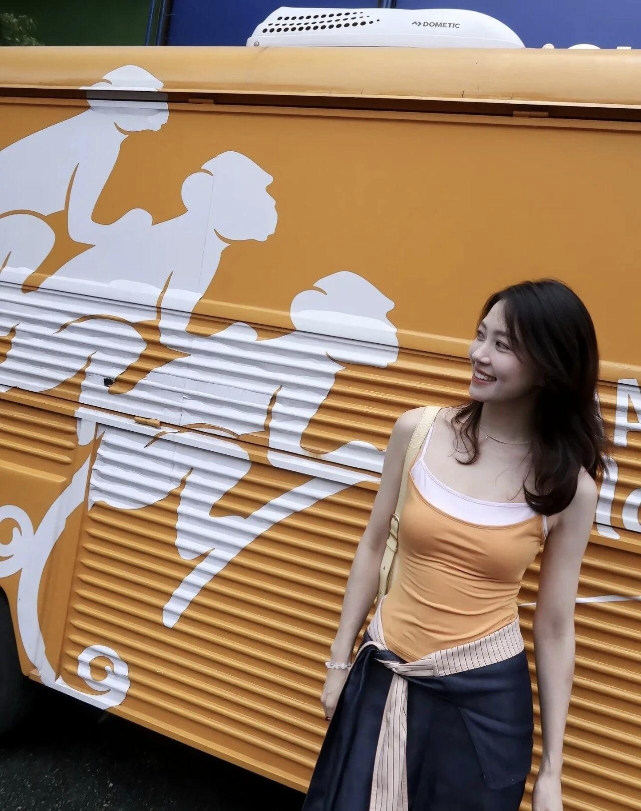 一个女孩靠在装饰有猴子的巴士旁微笑。