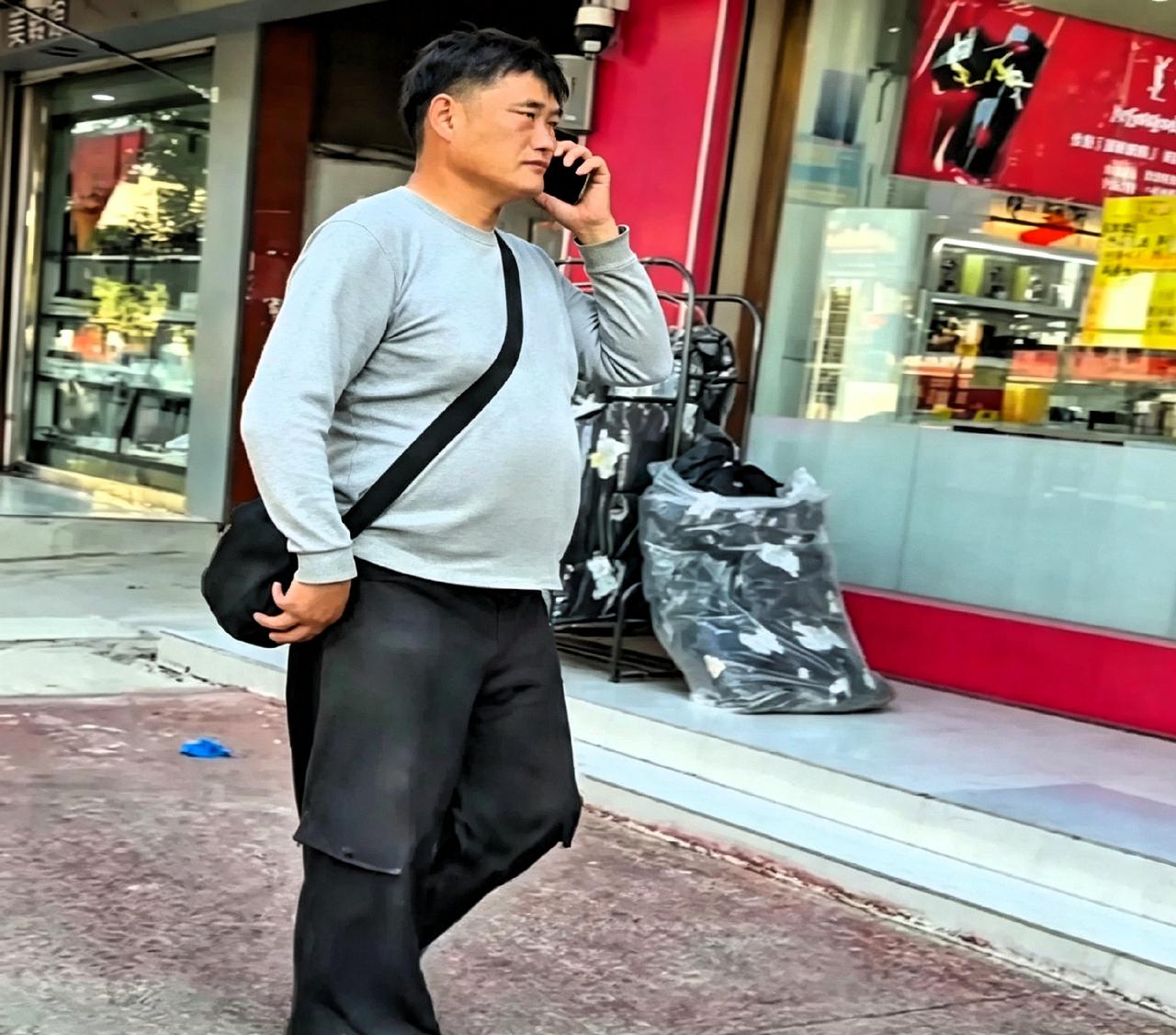 演出完回到老家，大衣哥背着黑包走在街上，边打电话边笑。灰上衣黑裤子，一点明星架子
