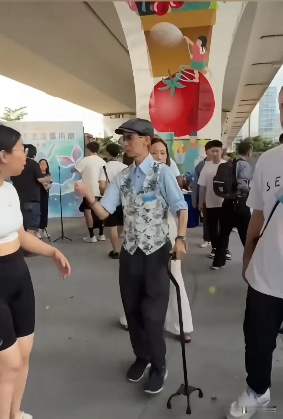 周星驰的御用配角张达明，近日现身参加活动，戴着帽子，穿着小马甲，拄着拐拐，走路蹒
