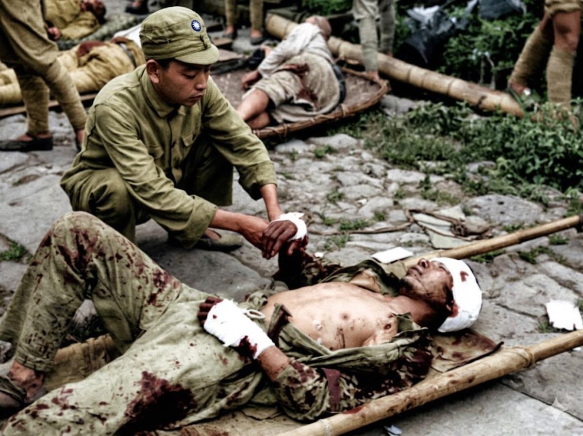 1944年，腾冲战役前线，年轻的卫生员蹲在地上，专注地为重伤士兵包扎手部伤口，神