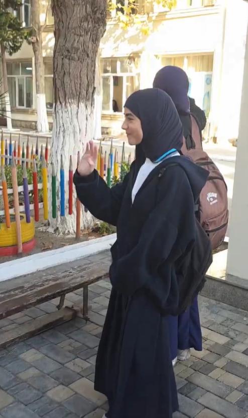 几名戴着头巾的阿塞拜疆女学生站在一栋建筑外，向里面的身穿校服的同学挥手并透过窗户
