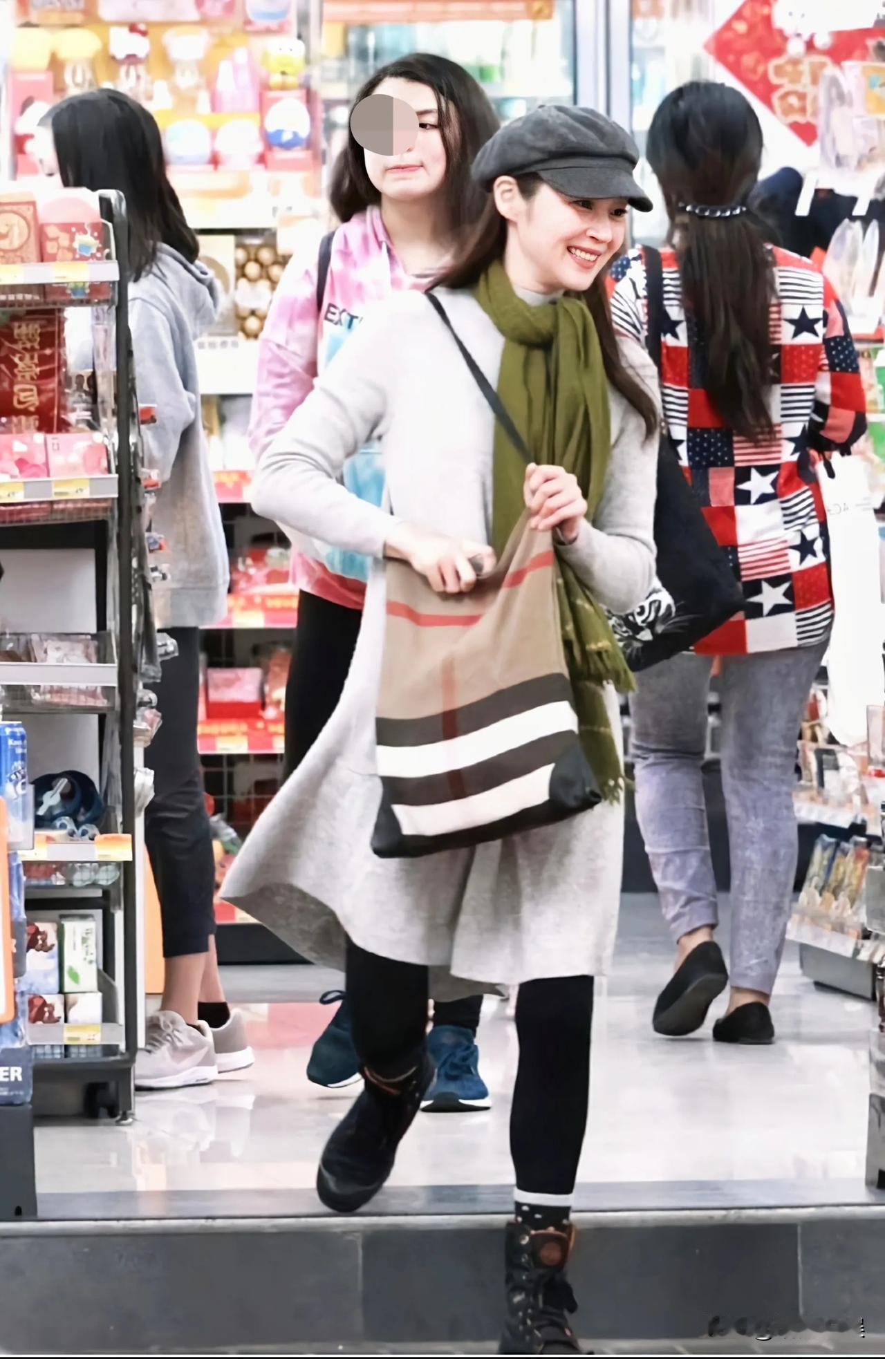 万绮雯在香港一家商场购物，围着绿色的围巾，戴着灰色帽子，穿着一件米白色冬裙，内搭