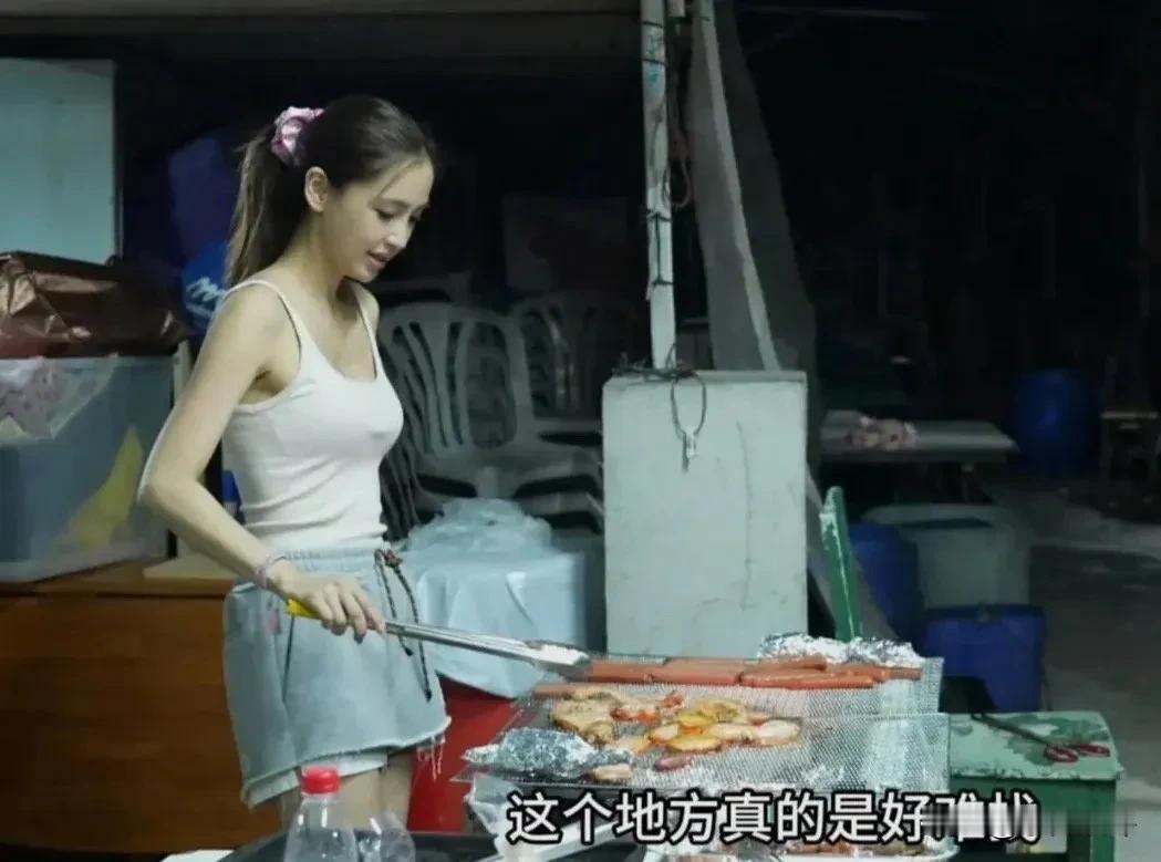 杨颖被路人拍到在户外亲自做烧烤，穿着吊带和牛仔短裤，素颜扎马尾，全程利落地翻动烤