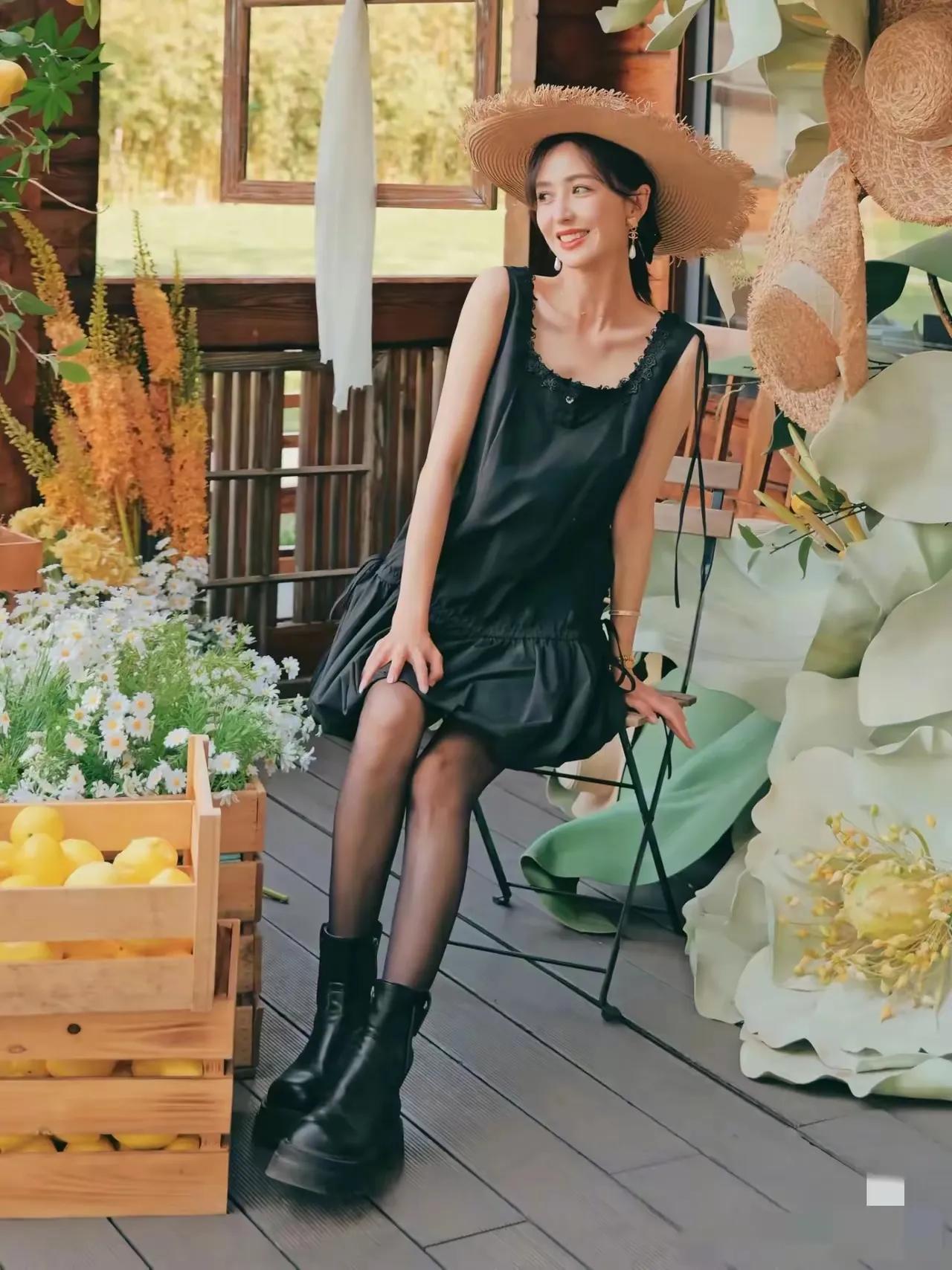 佟丽娅坐在木凳上，阳光洒在她的脸上，她微笑着，手里摇着扇子，旁边是装满鲜花的木箱