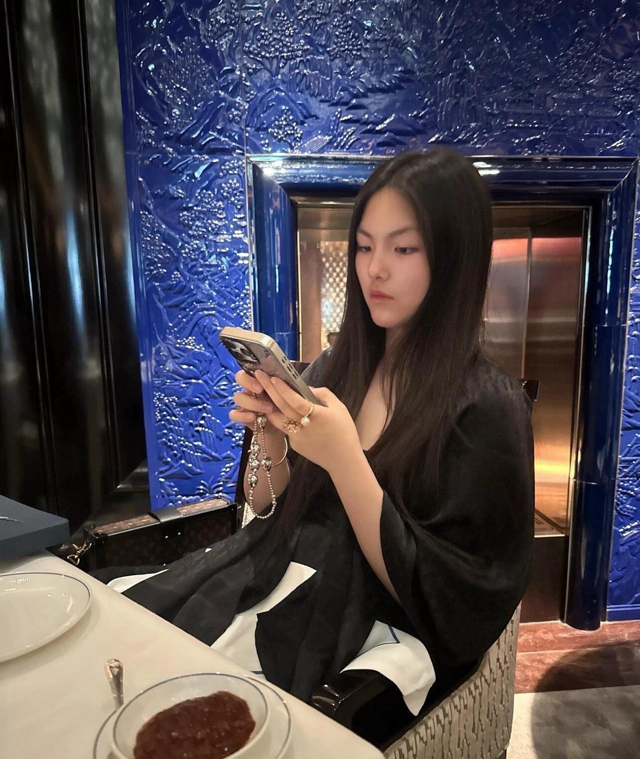 王诗龄假期休息做美甲，穿搭略显成熟～王诗龄身穿宽松黑色长袍连衣裙，手拎棕色花纹小