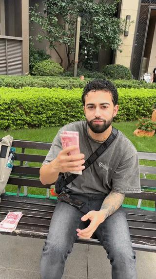 一名外国男子手上拿着大把的现金人民币坐在街头炫耀?他这是在炫富吗?其实外国人