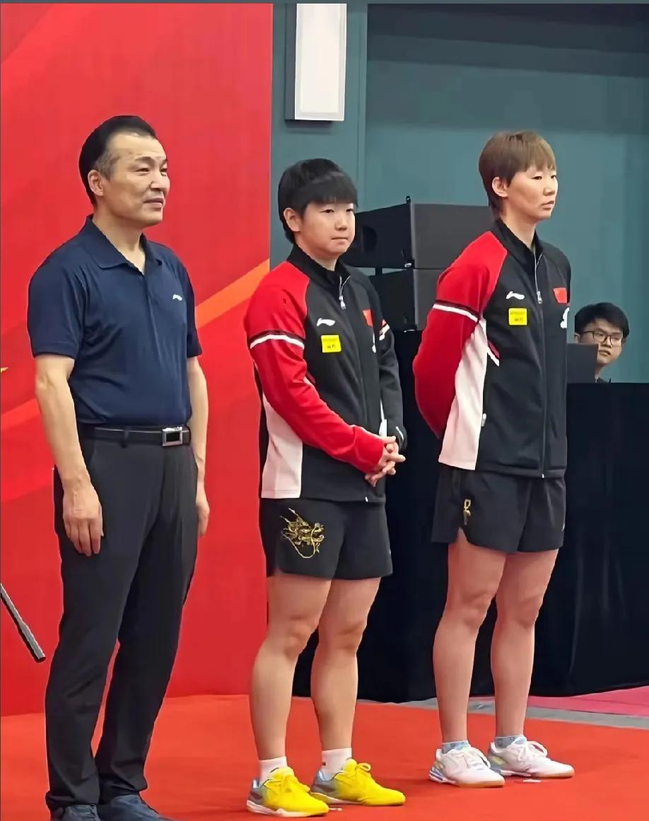 孙颖莎和王曼昱站在台上，一个向前，一个向后。她们的站姿，恰似她们竞技生涯的缩