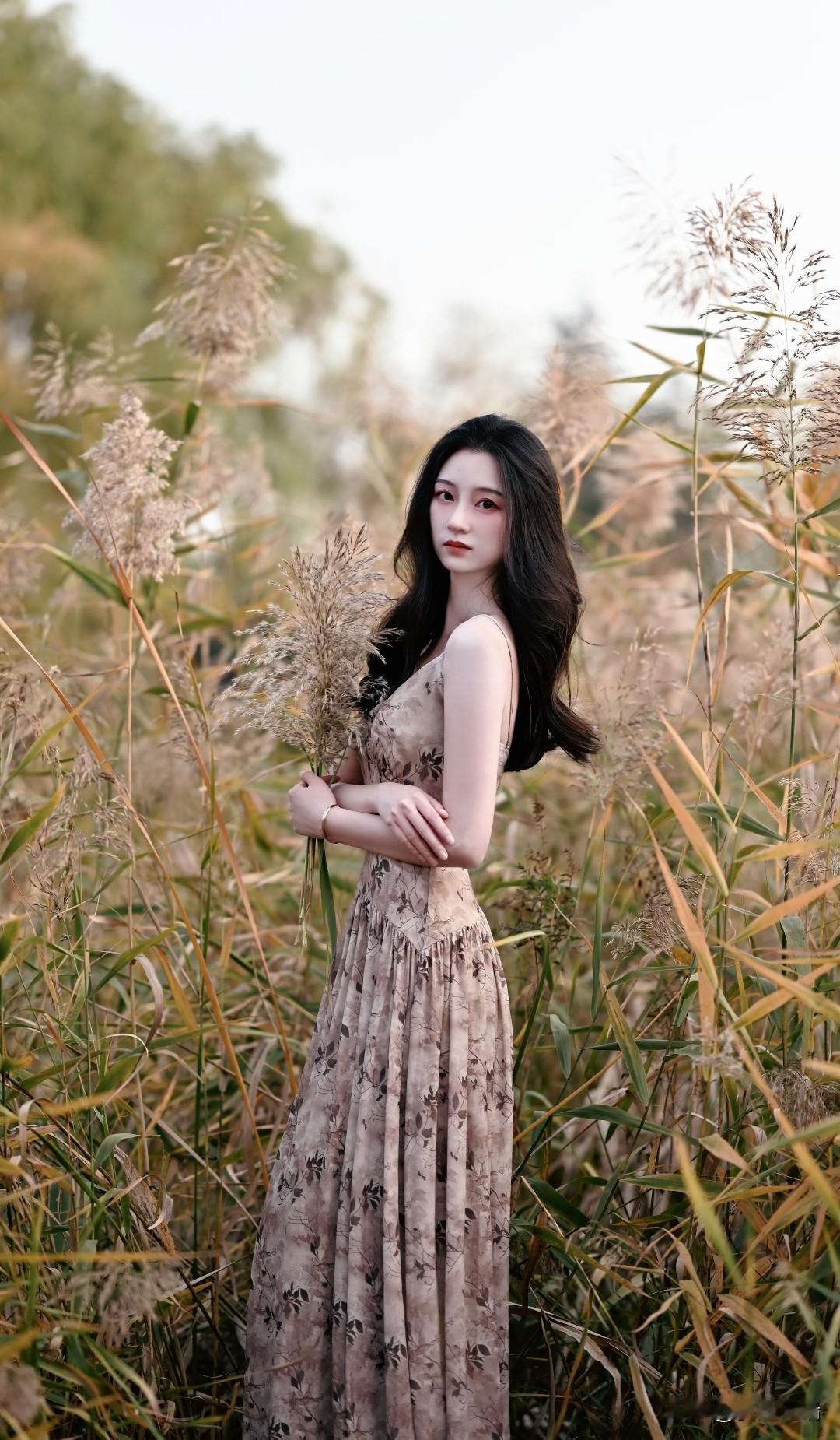 在秋日芦苇荡中，一位优雅的女子手持芦苇花，沉静而美丽。