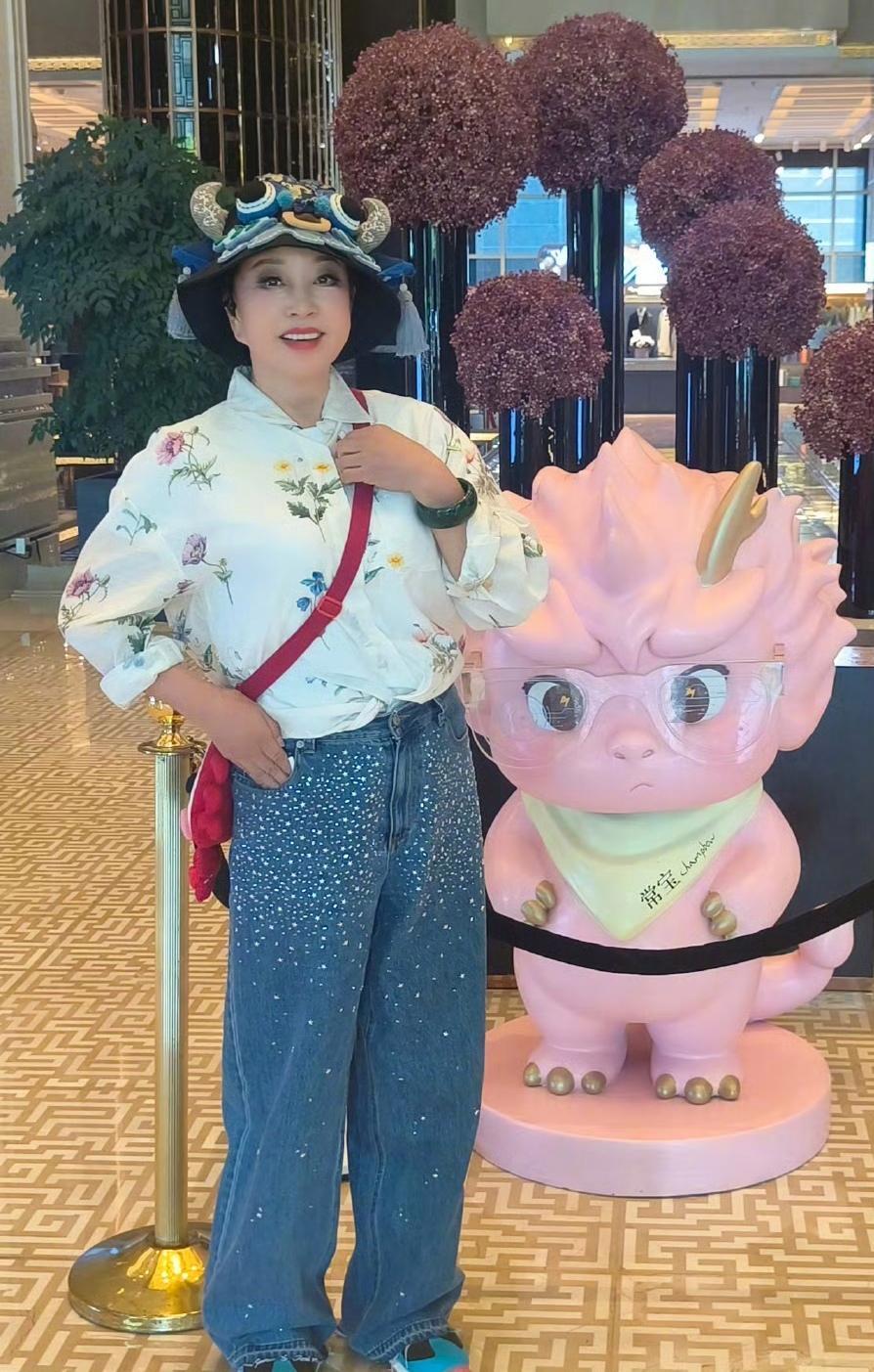 刘晓庆，穿了一件印花衬衫，配了一条有个性的牛仔裤，红色包包和帽子还有鞋子的搭配有
