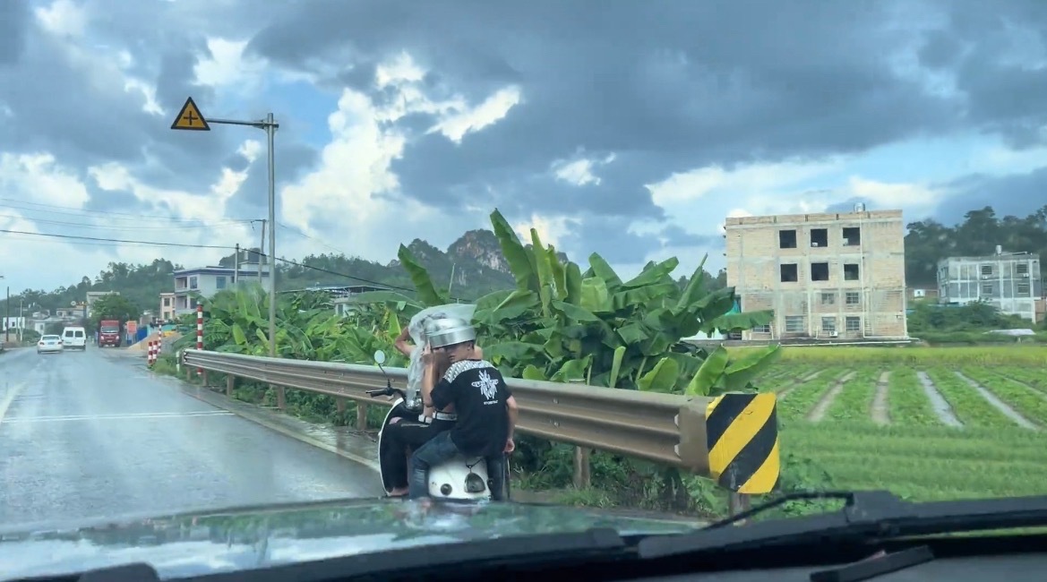 【玉林一电车后坐两名男子拿锅挡雨】近日，玉林市某乡镇道路上一辆电动车坐着3名男子