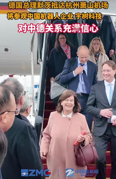 随德国总理一起来访问的这位大姨抢镜了。 她是第一个走下飞机的，胳膊上挎一个小