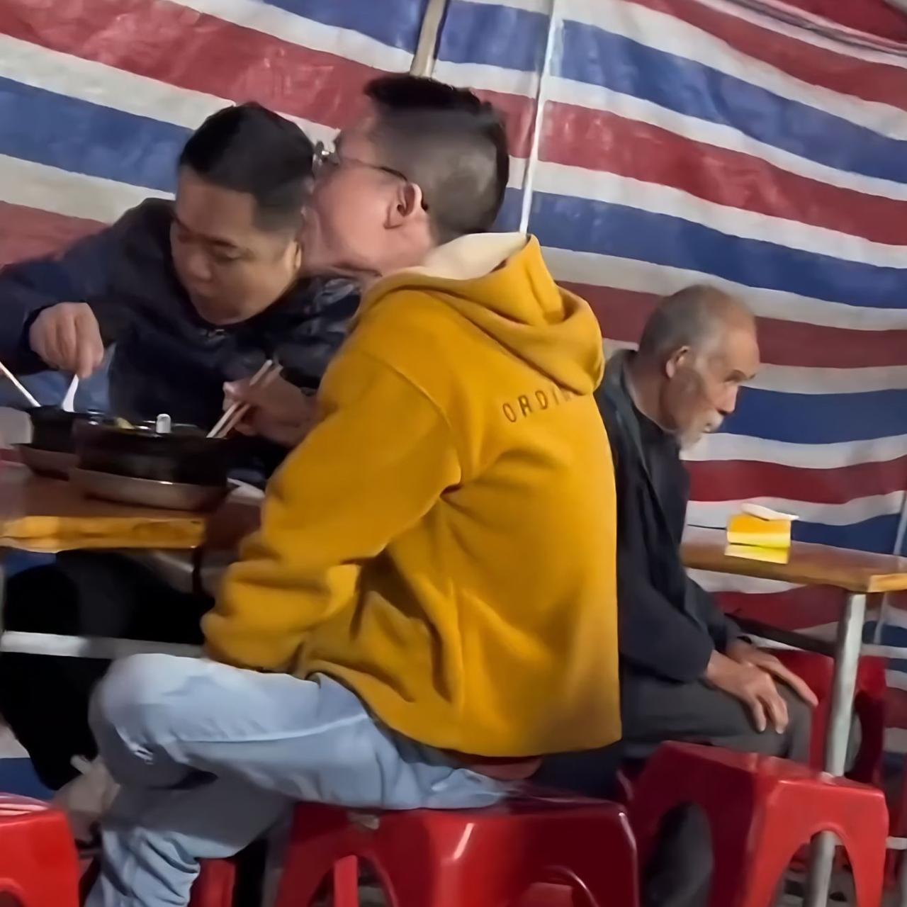 广西一宵夜摊，刚下班的男子与朋友正在吃夜宵的时候，突然看见邻桌有一位老人蹲在地上