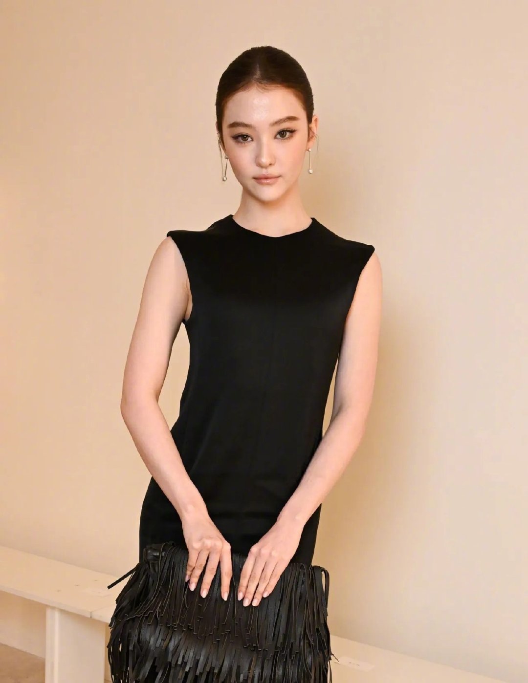 亮相COS2027春夏系列发布秀的身穿EllaGross，身穿黑色COS简洁款连衣裙，手拿包身缀满黑