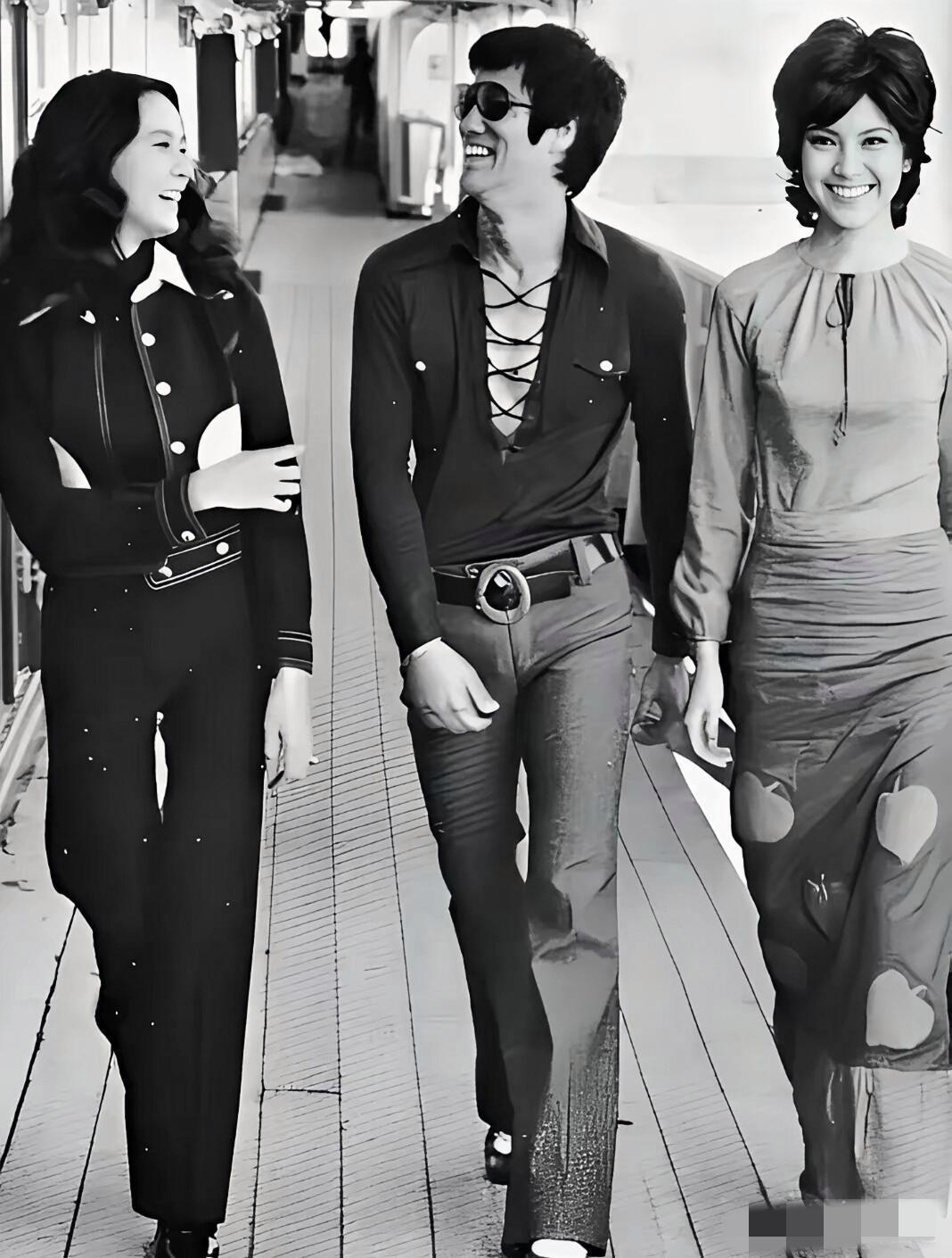 画面中的李小龙戴着墨镜，穿着修身黑衬衫，搭配高腰西裤，看上去笑意粲然，时尚有型，