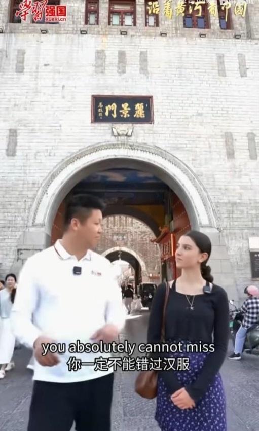 “学习强国”向外国女留学生讲解汉服。看背景，是河南洛阳的丽景门。女留学生是阿