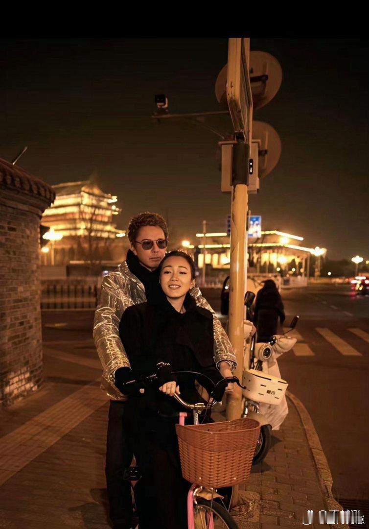 巩俐骑着自行车，带着丈夫穿行在北京街头，画面悠闲惬意，充满生活气息。