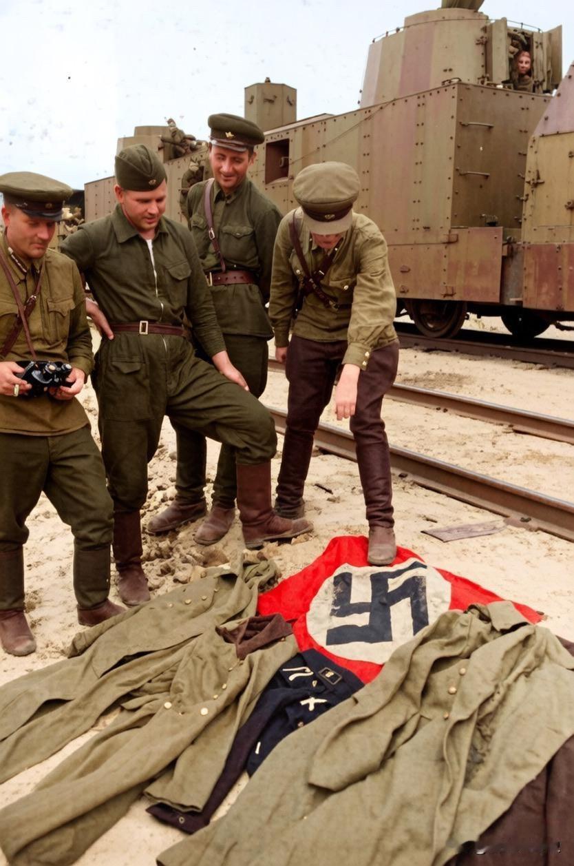 几名苏军正在查看他们的战利品，其中一名士兵一脚踩着一面纳粹旗帜。他们的身后是一列