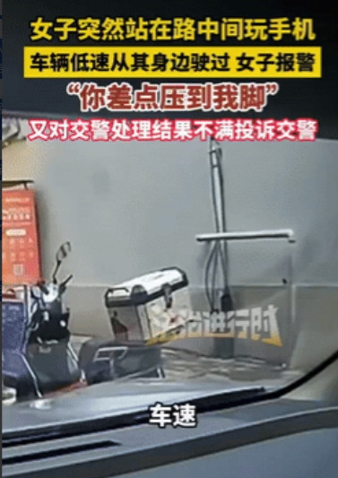 “小仙女又作妖了！”福建福州，一女子站在马路中间玩手机，旁边一辆轿车慢速经过，不