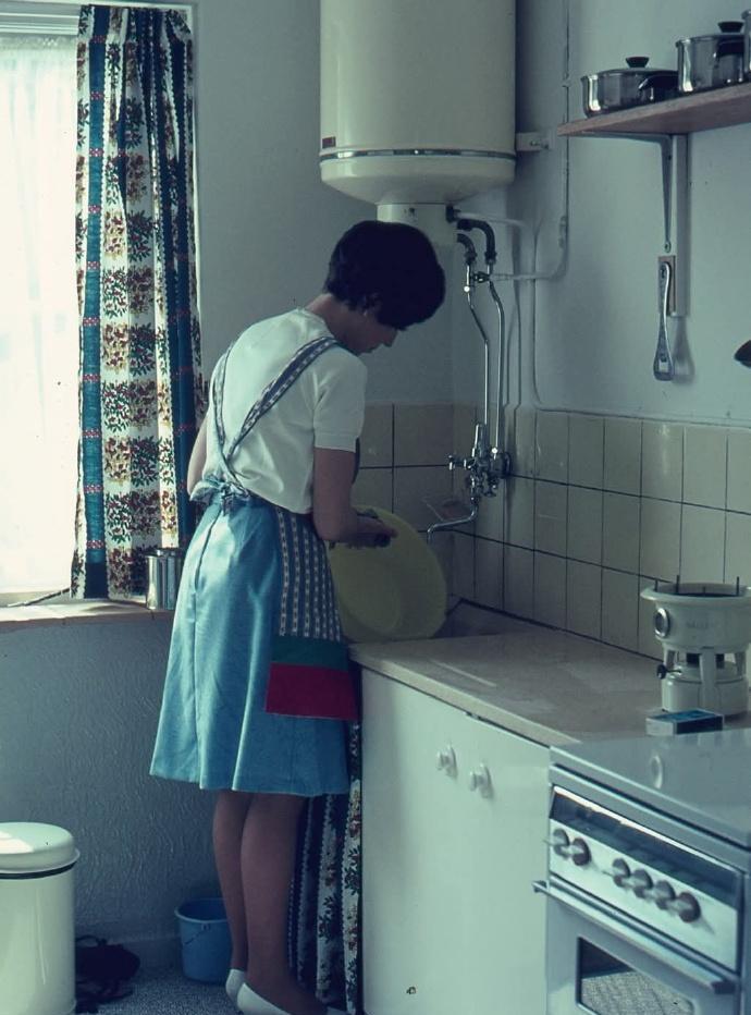 1968年，荷兰，一位家庭妇女在厨房里刷盆。妇女头顶上的那个连着着水龙头的电器应