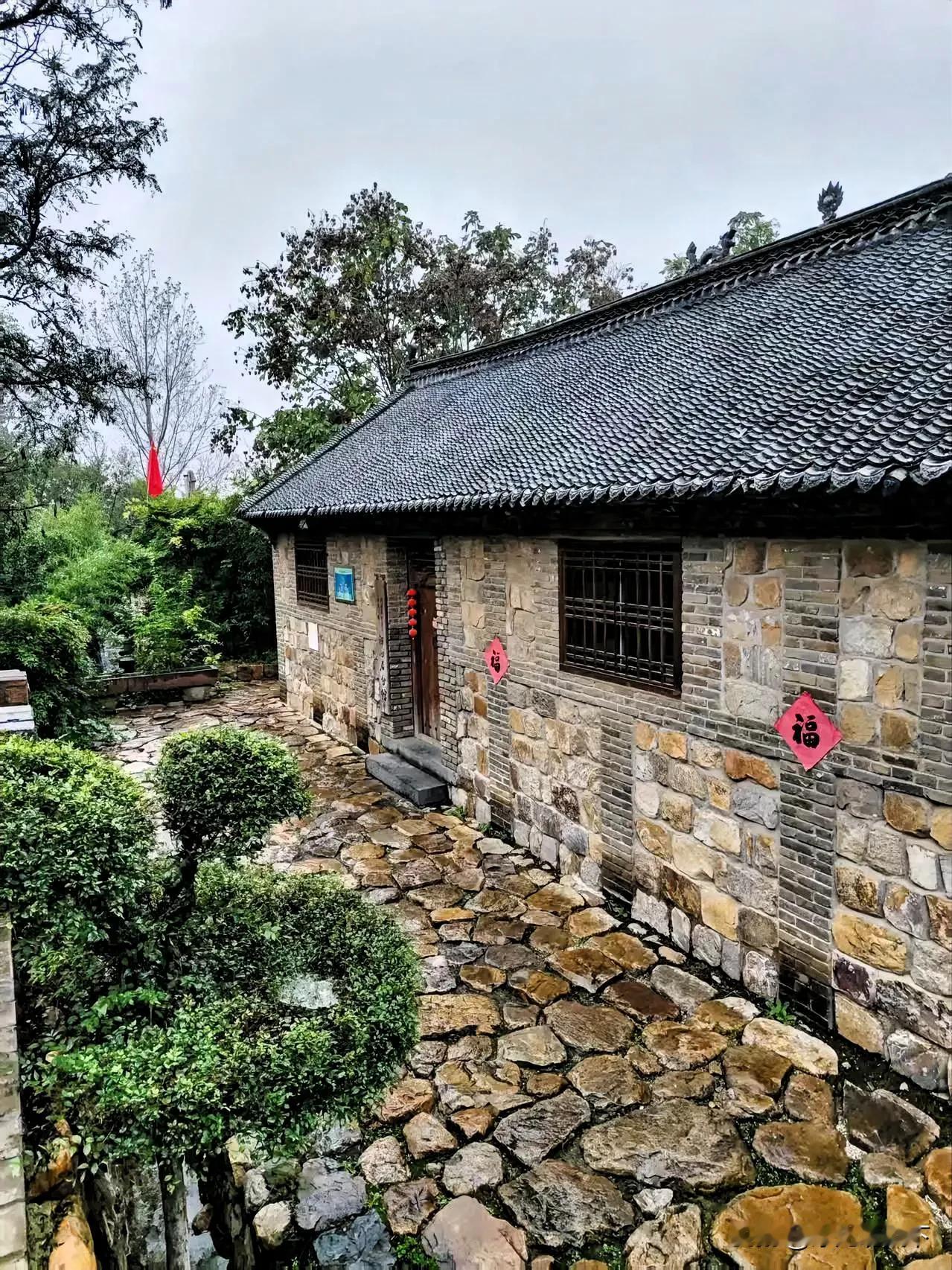 这里青砖石墙叠砌，黑瓦檐角微翘，这座隐于绿树间的石屋，是乡野里一首凝固的诗。