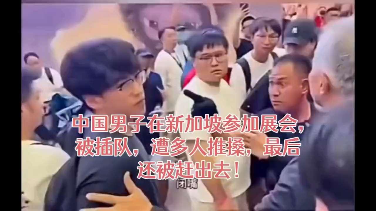 展会现场，中国小伙被工作人员指着鼻子吼。旁边一群人围着他推搡，他一边后退一边试图