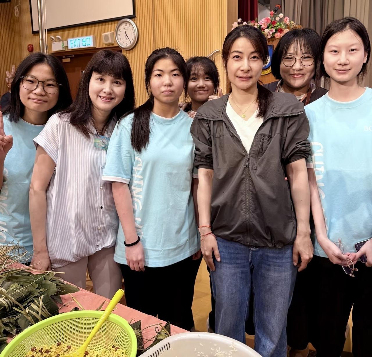 郭晶晶与学生们一起包粽子，手上系着红色手绳，穿着补素，不施粉黛，大方美丽