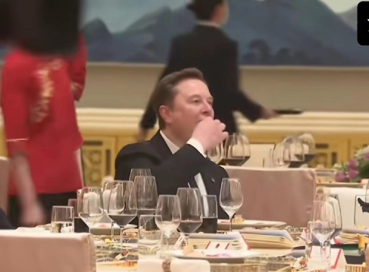 马斯克真饿了，欢迎晚宴还没正式开始，坐在座位上，直接上手捏着吃了，好像是一块点心