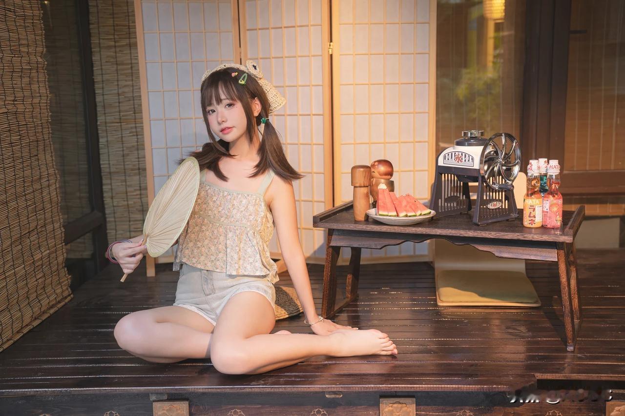 双马尾的她盘腿而坐，米白色蒲扇掩不住那份俏皮；草帽下的她赤脚交叠，折扇轻点间尽显