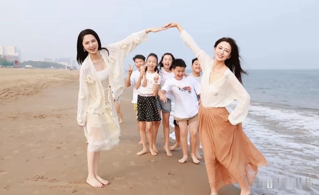 董璇佟丽娅又带着娃来阿那亚海边玩啦。两位妈妈一身白色防晒衫，在沙滩上手拉手搭成拱门，小朋友们排好队，