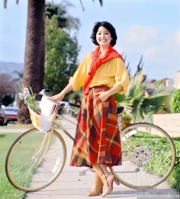一张摄于1980年美国加州的老照片，照片中的推着一件自行车的女子是邓丽君，她长相