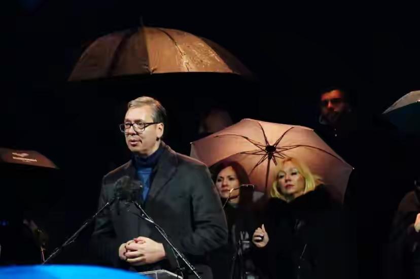 武契奇讲话，伞抢镜了。既没太阳又没下雨，他们撑伞这是为何？
