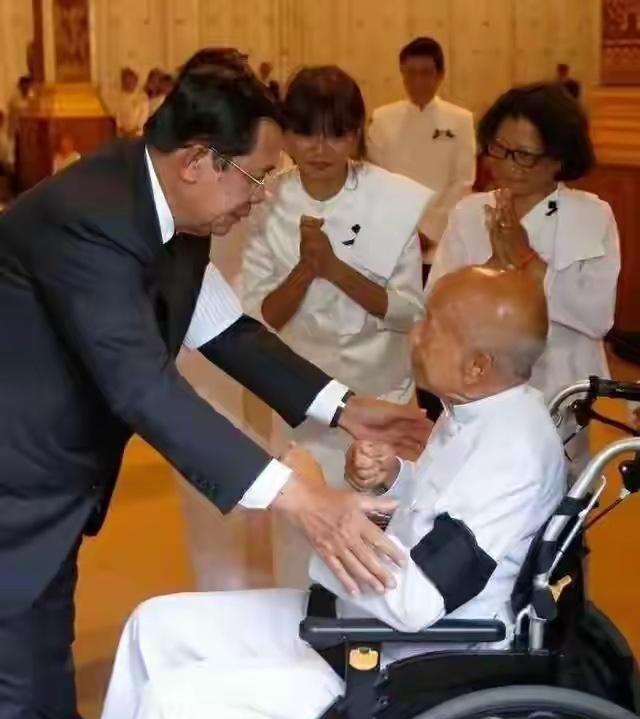 就是这张照片，信息量极大。镜头前，洪森弯下腰，伸出手，握住轮椅里拉那烈亲王那只消