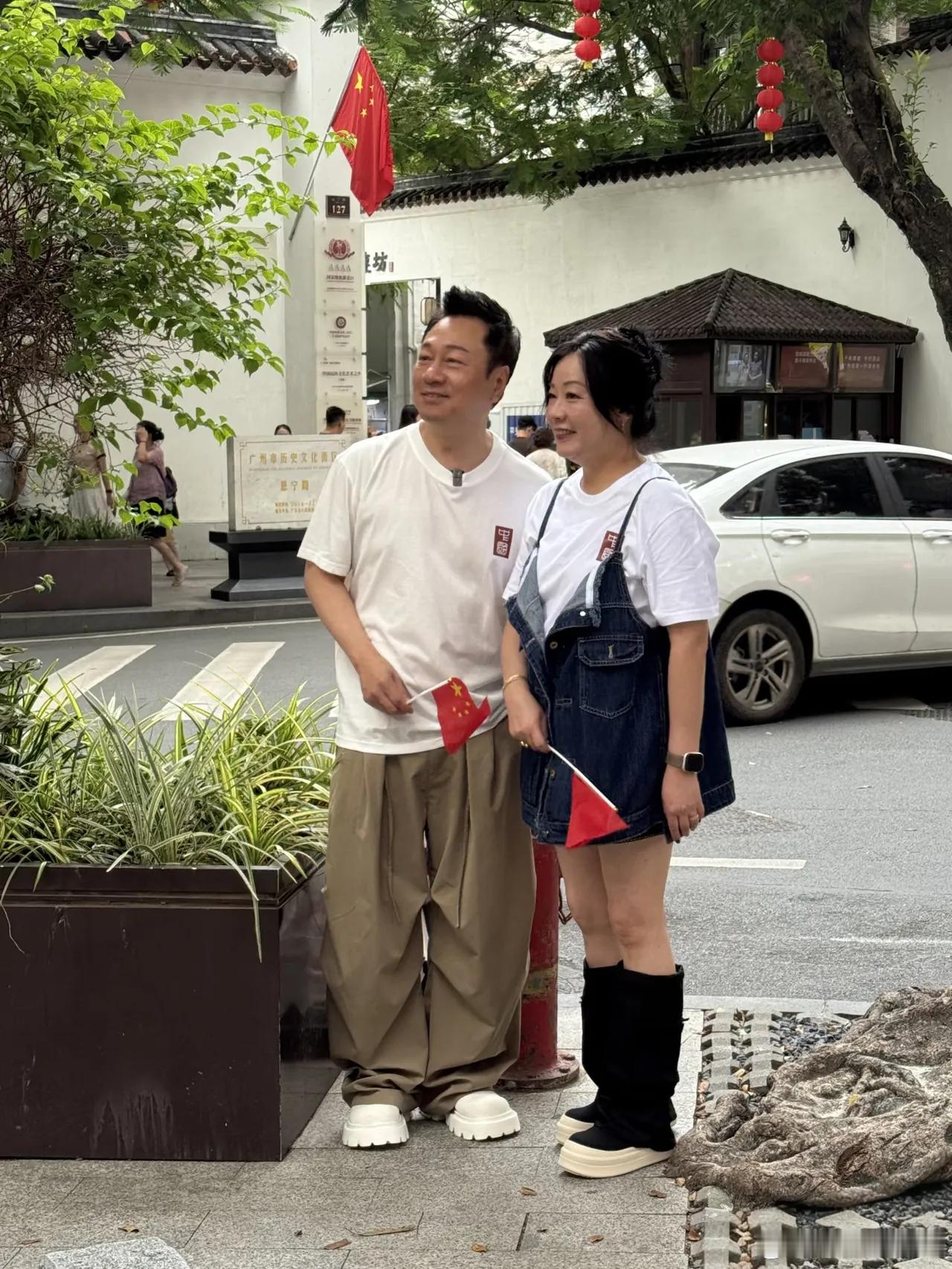 黎耀祥与妻子梁耀莲现身广州永庆坊，夫妻俩手持小五星红旗，满脸笑意地感受着节日氛围