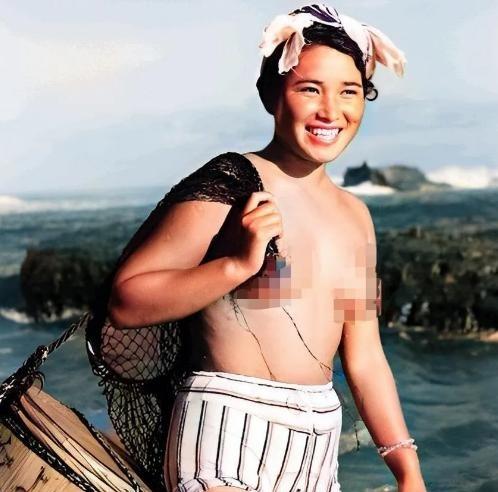 1955年，一名身体强壮的日本女人赤裸上半身，背着一个黑色的编织袋站在海边。这个