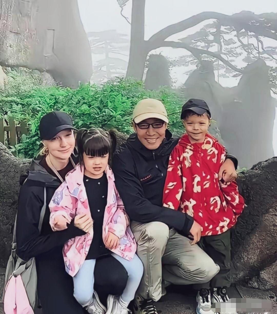 撒贝宁一家四口在黄山迎客松旁留念的合影：妻子李白头戴黑色棒球帽、穿户外黑衣，神